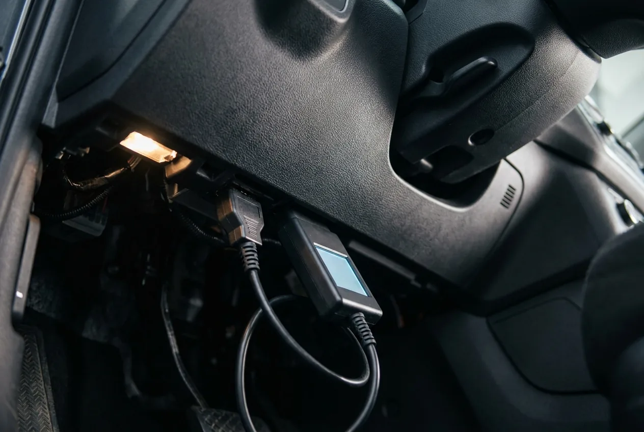 A diagnostic tool plugged into the OBD port under the dashboard, seen from the driver's footwell